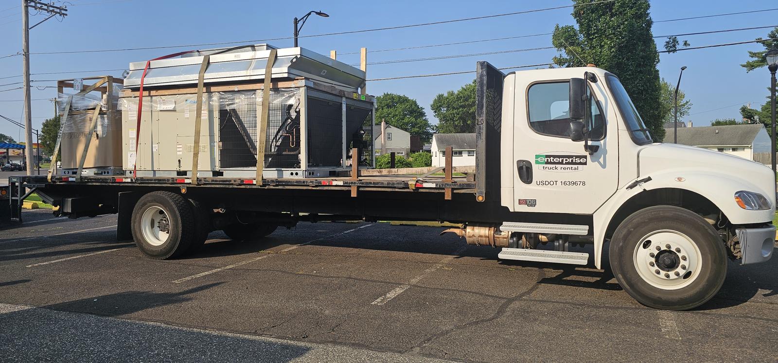 Flatbed truck delivering a new packaged rooftop HVAC unit to a job site