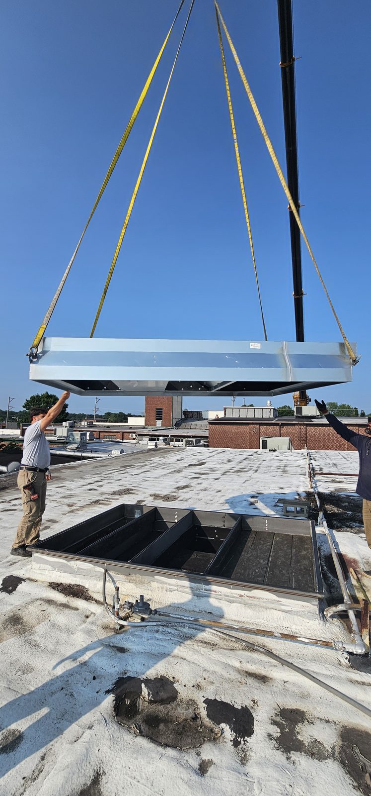 Crane lifting a structural support beam into place for a new rooftop unit curb