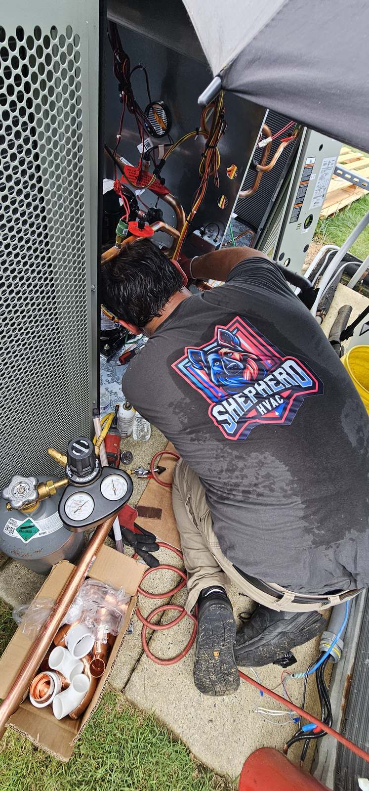 Shepherd HVAC technician working inside an open condensing unit with gauges connected