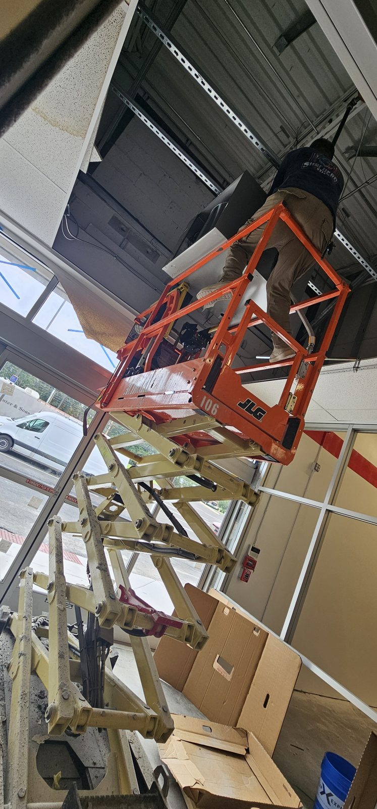 Scissor lift positioned for overhead HVAC installation inside a commercial space