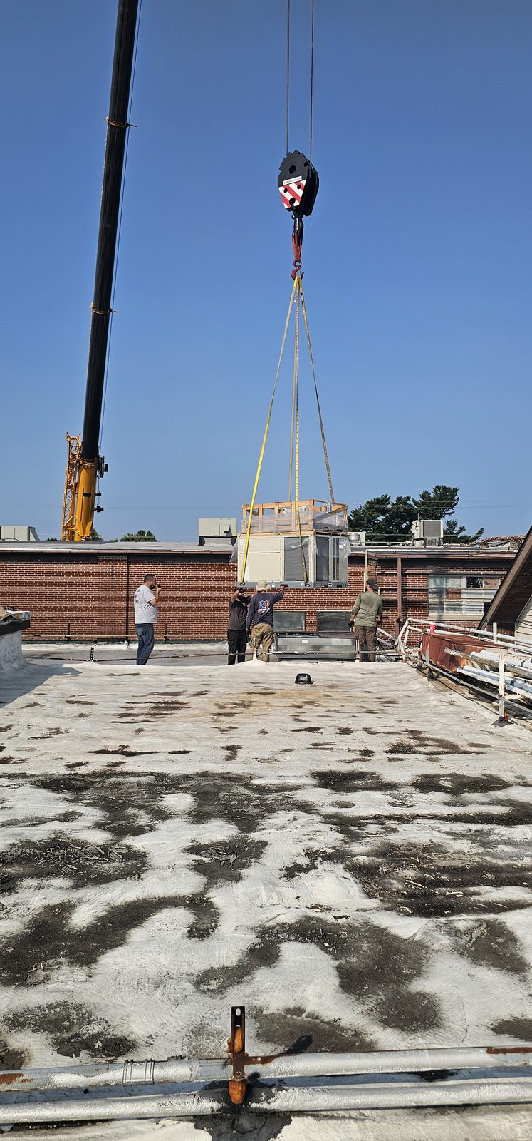 Crane hook descending to a commercial roof to remove an old packaged unit