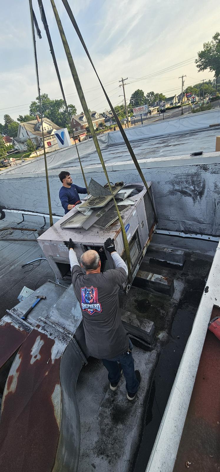 Crane lowering a packaged HVAC unit onto the roof while a Shepherd HVAC technician guides it