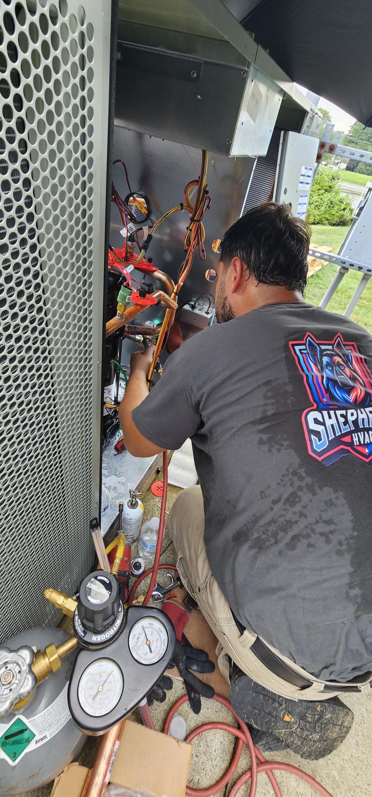 Shepherd HVAC technician taking refrigerant readings with manifold gauges at a condensing unit